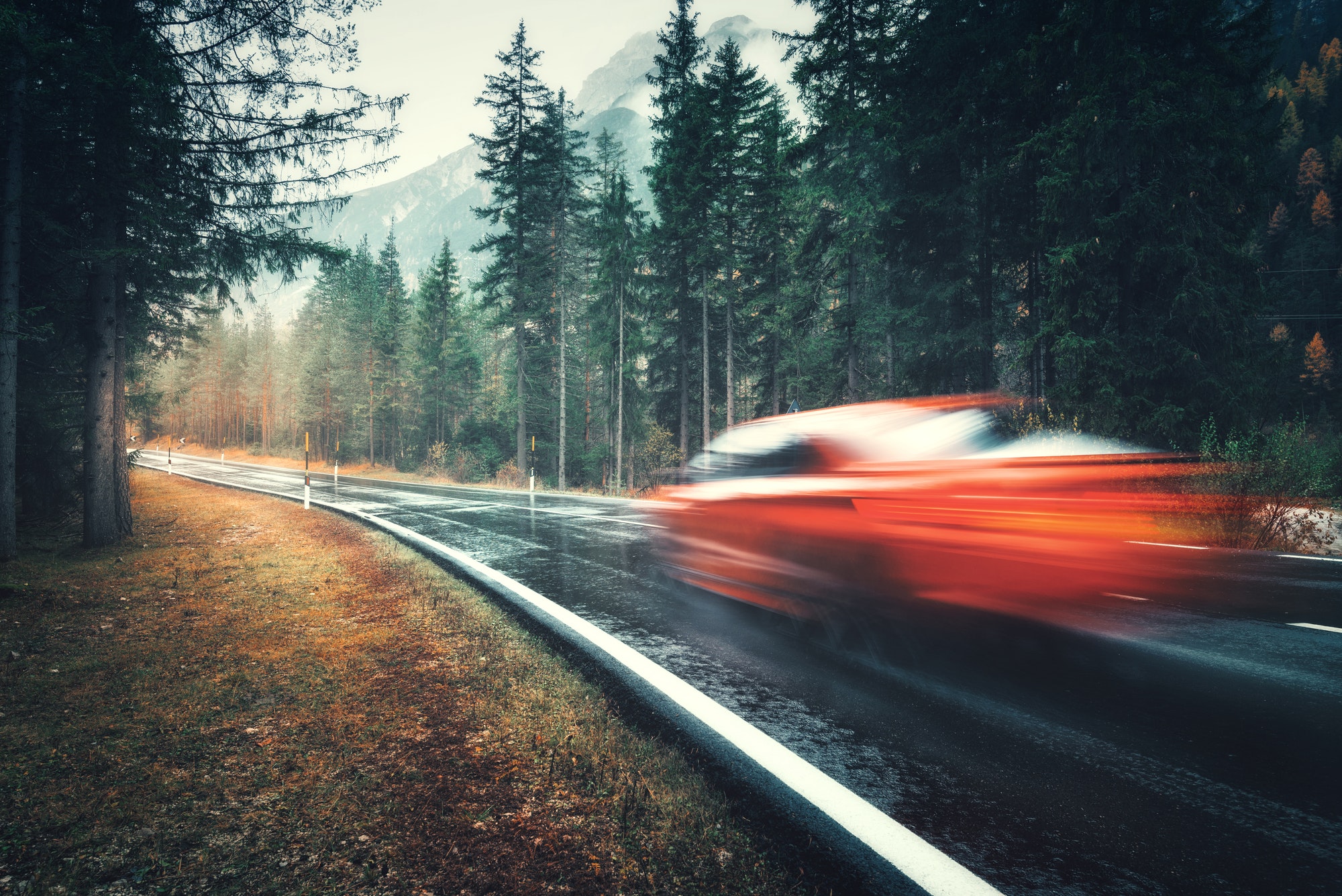 Blurred red car in motion on the road in autumn forest